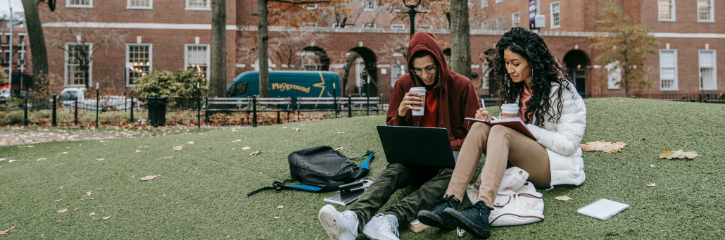 two college students on campus lawn looking at laptop - Fireline Broadband