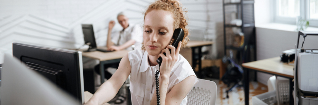 woman making a phone call using business desk phone - AI to fight spam - Fireline Broadband